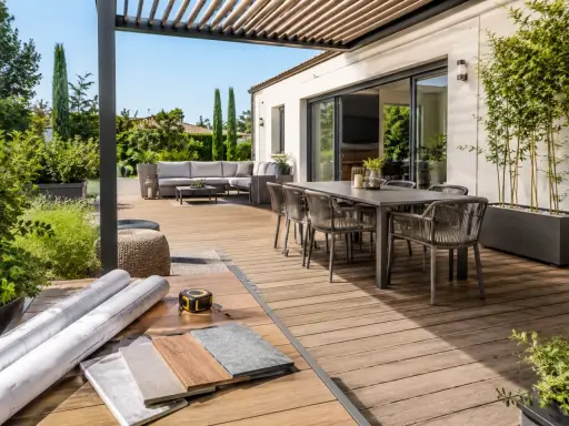 Aménagement d'une **terrasse en L** moderne avec salon extérieur, table à manger et matériaux de construction.