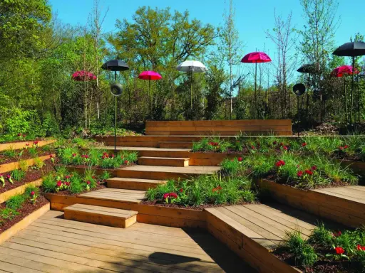 Aménagement de jardins avec terrasses en bois, parterres fleuris et parasols colorés.