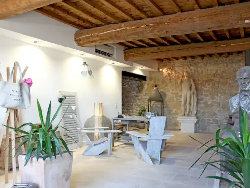 Salon moderne avec poutre apparente. Deux fauteuils en bois, une table, des plantes et des statues ornent cet espace chaleureux.
