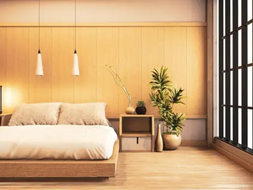 Une chambre style japonais épurée avec un lit bas en bois, des coussins douillets, des plantes vertes et une fenêtre aux persiennes sombres.