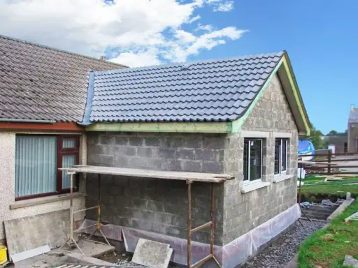 Agrandissement maison sur le côté en cours de construction, murs en parpaings, nouveau toit gris, échafaudage.
