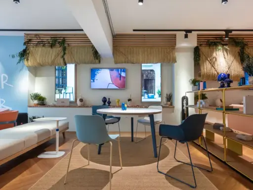 Ambiance lumineuse et colorée pour une idée décoration bureau professionnel. Canapés, table ronde, étagères et plantes créent un espace accueillant.