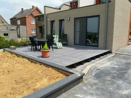 Terrasse avec dalles grises sur plots, prête à accueillir une dalle béton. Table et chaises sur le côté.