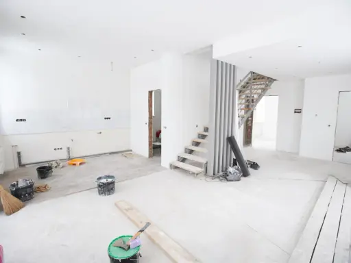 Chantier en cours pour rénover ma maison : escalier, seaux de peinture, balai et matériaux au sol.