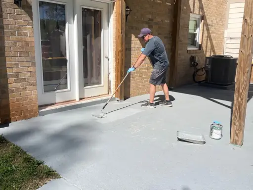 Homme appliquant une peinture sur mur béton extérieur avec un rouleau. Le sol de la terrasse est en cours de rénovation.