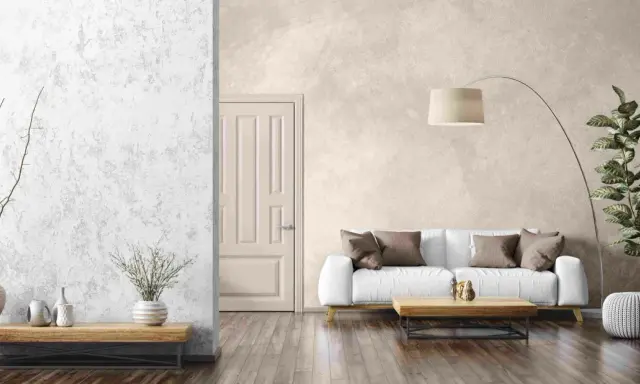 Salon moderne avec un canapé blanc, une table basse en bois et un grand pot de fleurs. Le mur de fond présente un bel **effet enduit décoratif** texturé.