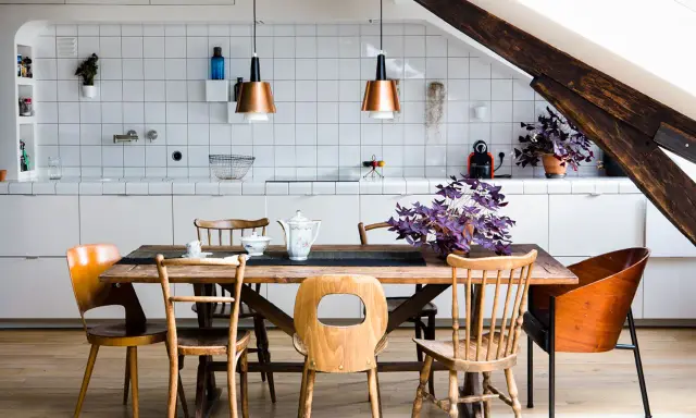 Une cuisine ouverte sur salle à manger avec un îlot central, des chaises en bois et des suspensions cuivrées.