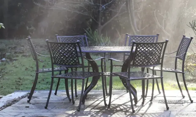 Un ensemble de mobilier de jardin résistant aux intempéries, une table et quatre chaises en métal, est mouillé par la rosée matinale.