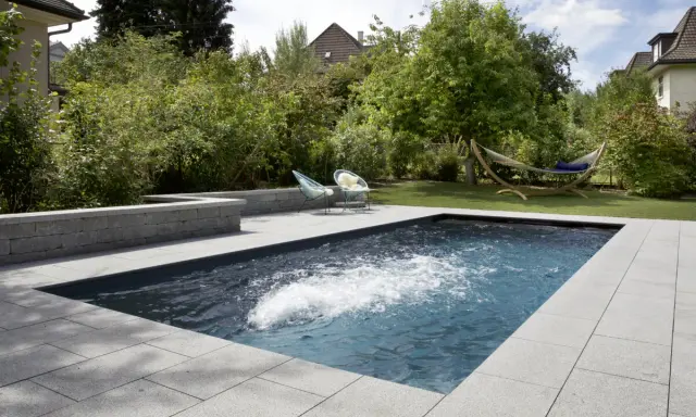 Aménagement paysager d'une piscine creusée avec terrasse en pierre, deux chaises bleues et un hamac invitant à la détente.