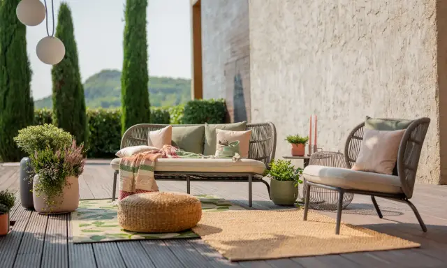 Aménagement terrasse extérieure : un canapé et un fauteuil confortables, des coussins, un plaid coloré, des plantes et des tapis invitent à la détente.