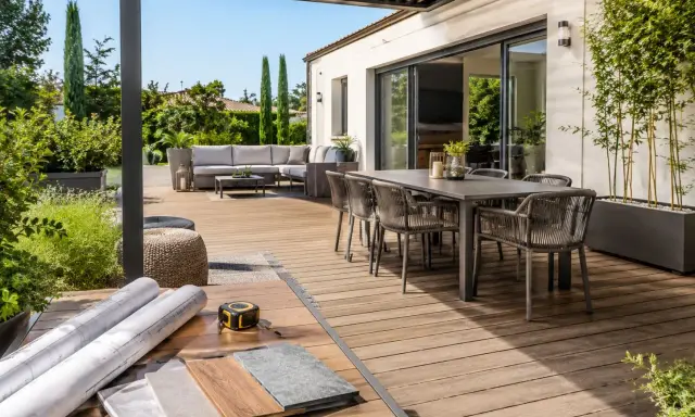 Aménagement d'une **terrasse en L** moderne avec salon extérieur, table à manger et matériaux de construction.