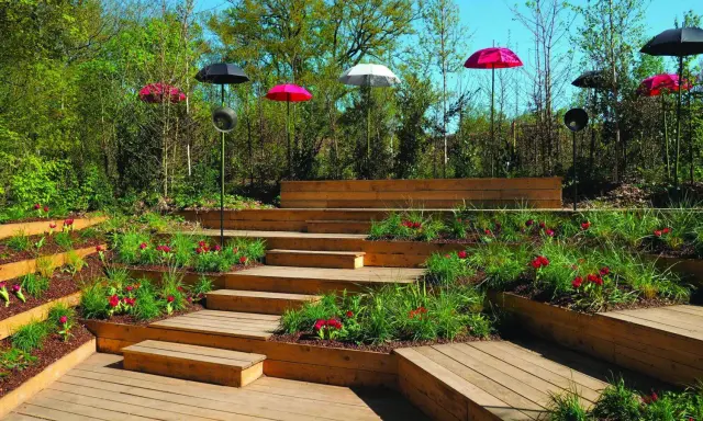 Aménagement de jardins avec terrasses en bois, parterres fleuris et parasols colorés.