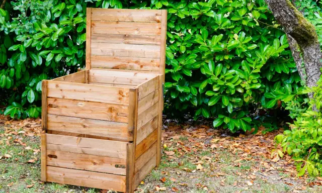 Un composteur en bois, prêt à l'emploi, est installé dans un jardin verdoyant. Idéal pour fabriquer un composteur maison.