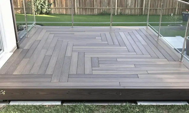 Une belle terrasse bois sur plot béton, avec un motif en chevrons élégant et une balustrade en verre moderne.
