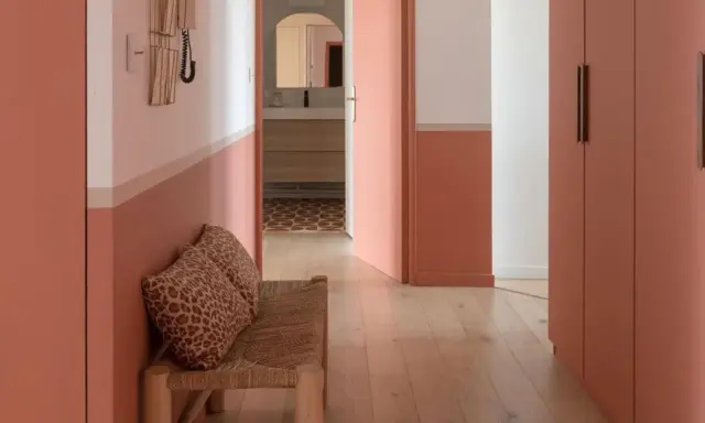 Banc en rotin avec coussins léopard, murs bicolores corail et blanc, portes roses. Une belle idée déco couloir moderne.