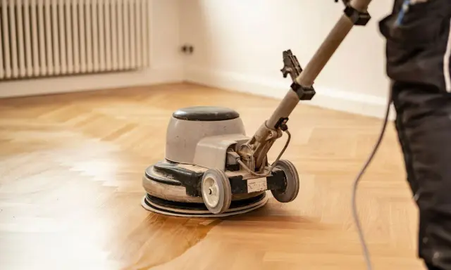 Polissage d'un parquet ancien avec une ponceuse. La rénovation redonne tout son éclat au bois.