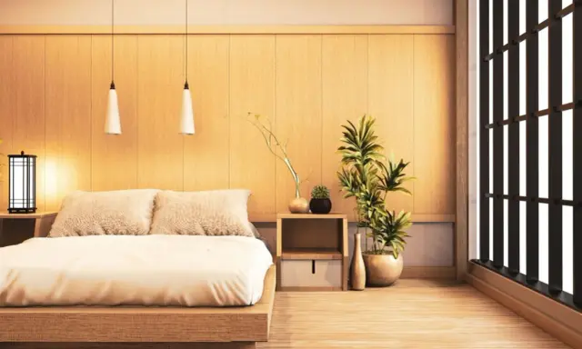 Une chambre style japonais épurée avec un lit bas en bois, des coussins douillets, des plantes vertes et une fenêtre aux persiennes sombres.