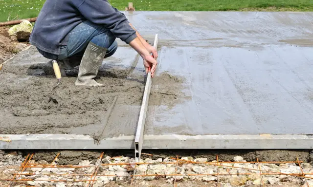 Un ouvrier ajuste le coffrage d'une dalle en béton frais avec une règle de maçon.
