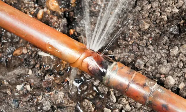 Une fuite sur un tuyau de cuivre, l'eau jaillit d'une fissure dans le sol.