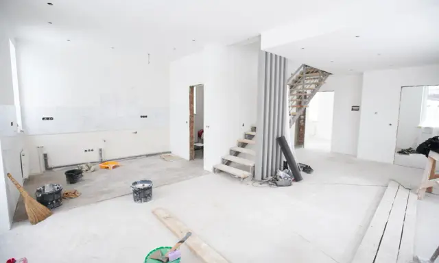 Chantier en cours pour rénover ma maison : escalier, seaux de peinture, balai et matériaux au sol.