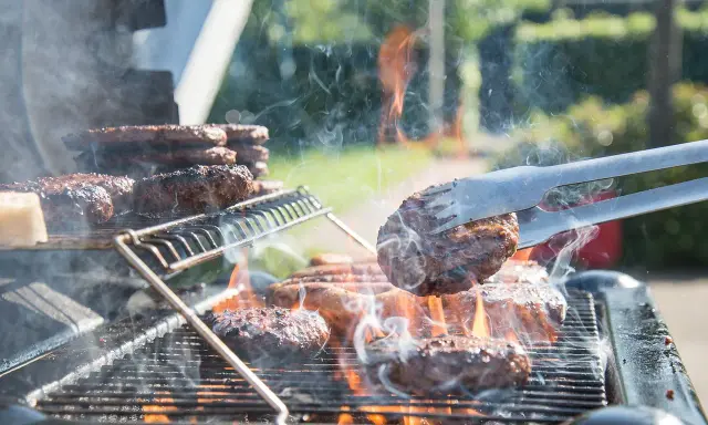 Des hamburgers grillent sur un barbecue à gaz. La cuisson est intense, la fumée s'élève. Nettoyer barbecue gaz après ce festin sera nécessaire.