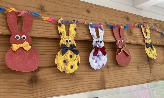 Guirlande de lapins colorés, déco de Pâques à faire soi-même avec récup. Des lapins en papier aux motifs variés, ornés de nœuds et d'yeux mobiles, suspendus à une ficelle multicolore.