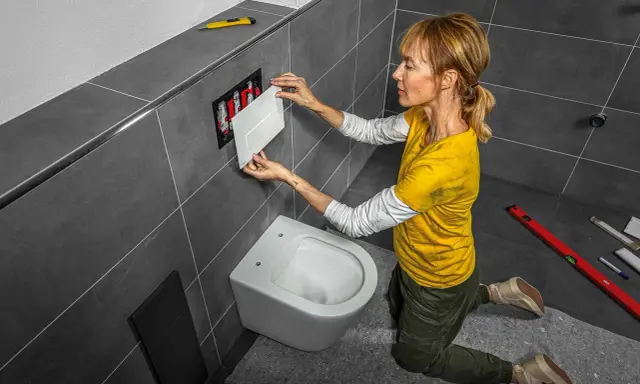 Une femme installe une plaque de commande pour changer la chasse d'eau d'une nouvelle cuvette de toilette suspendue.