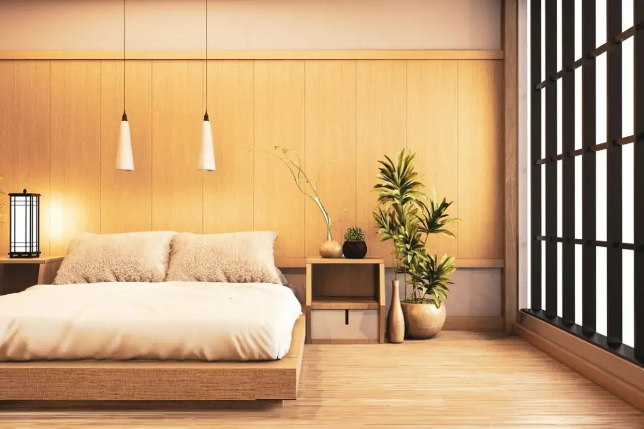 Une chambre style japonais &eacute;pur&eacute;e avec un lit bas en bois, des coussins douillets, des plantes vertes et une fen&ecirc;tre aux persiennes sombres.
