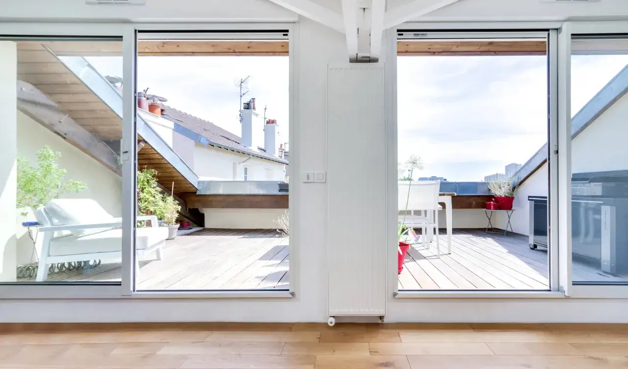 Vue sur terrasse am&eacute;nag&eacute;e avec mobilier blanc, barbecue et toits. Le cout am&eacute;nagement combles est optimis&eacute; pour ce style de vie.