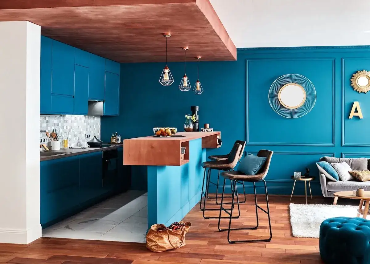 Cuisine moderne aux meubles bleu canard, avec un îlot central en bois et des tabourets de bar. Le plafond en cuivre ajoute une touche chaleureuse.