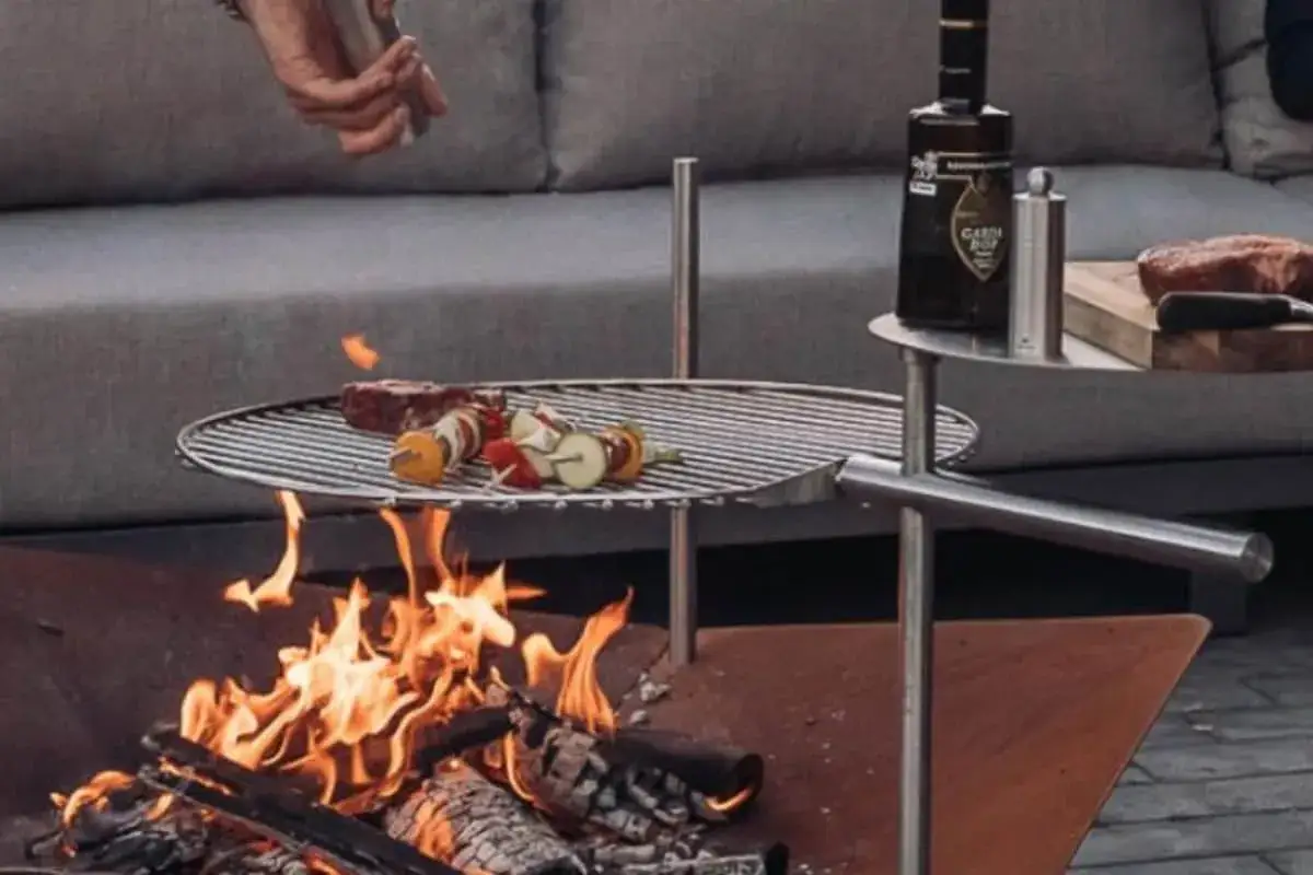Un homme prépare à faire un barbecue, avec des brochettes et un steak sur le gril au-dessus des flammes.