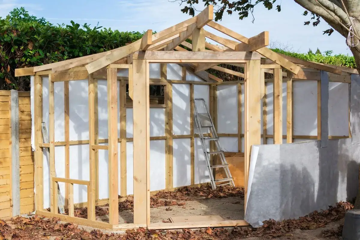 Structure en bois d'une cabane de jardin en construction, avec un toit en cours d'installation et une &eacute;chelle &agrave; l'int&eacute;rieur.