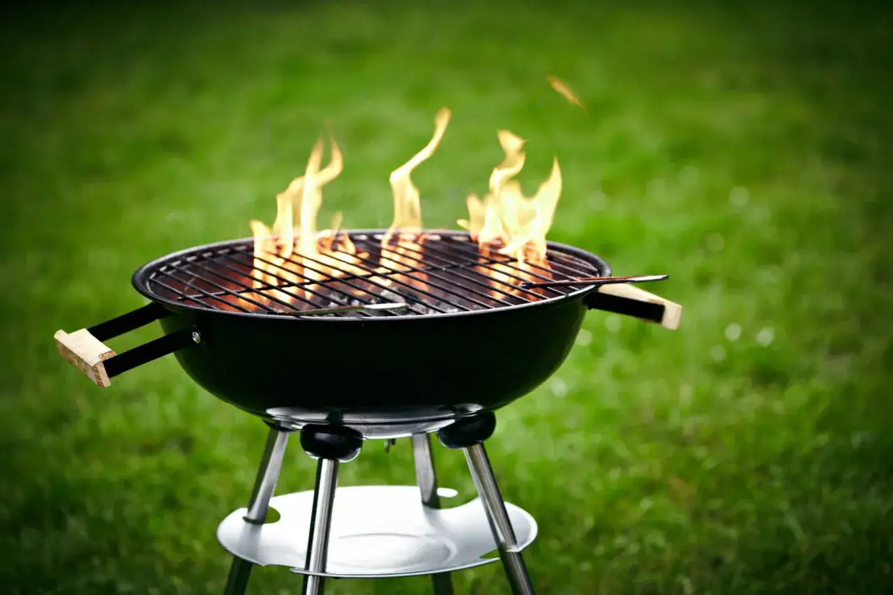 Un barbecue en plein air, prêt à l'emploi. Les flammes dansent sur la grille, signe qu'il est temps de penser à comment allumer un barbecue pour un repas convivial.
