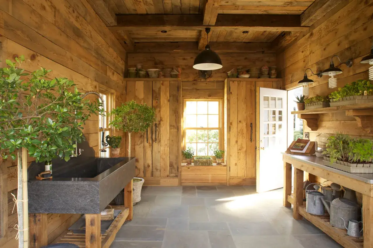 Aménagement abri de jardin rustique avec évier en pierre, étagères chargées de plants et outils de jardinage.