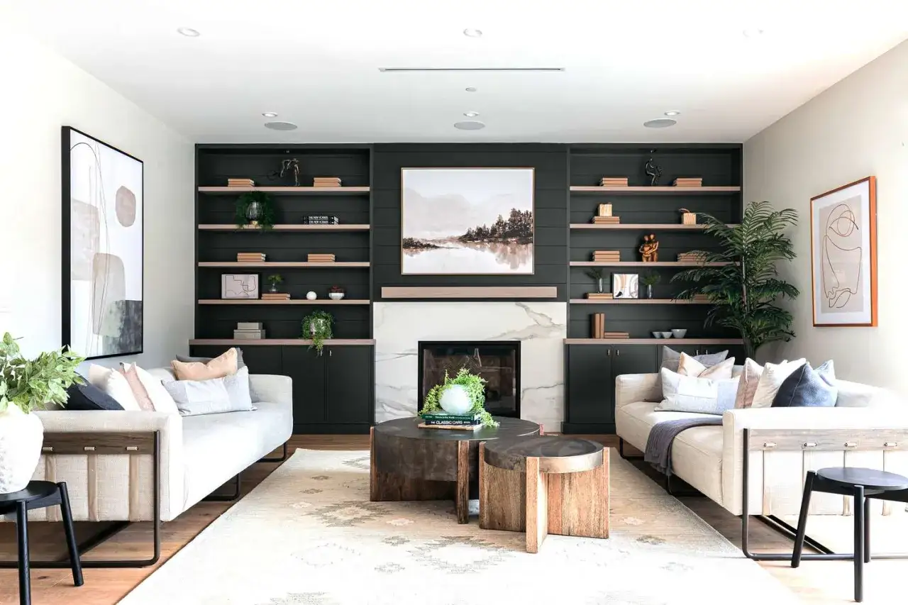 Un salon moderne avec des canapés beiges, une cheminée en marbre et des étagères vert foncé. Le beige et le bois clair s'accordent bien avec le vert foncé.