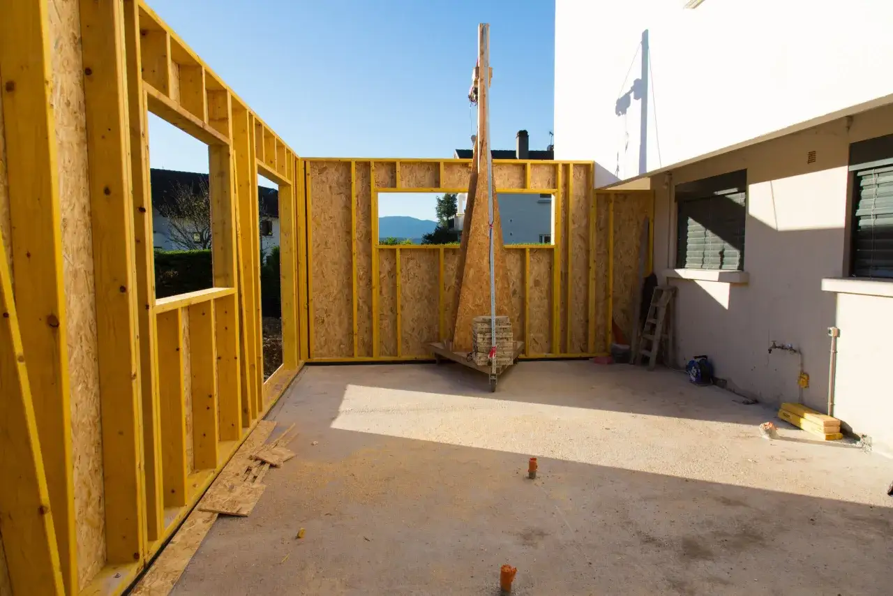 Structure en bois pour agrandissement maison sur le c&ocirc;t&eacute;. Le chantier est en cours, avec des mat&eacute;riaux de construction visibles.