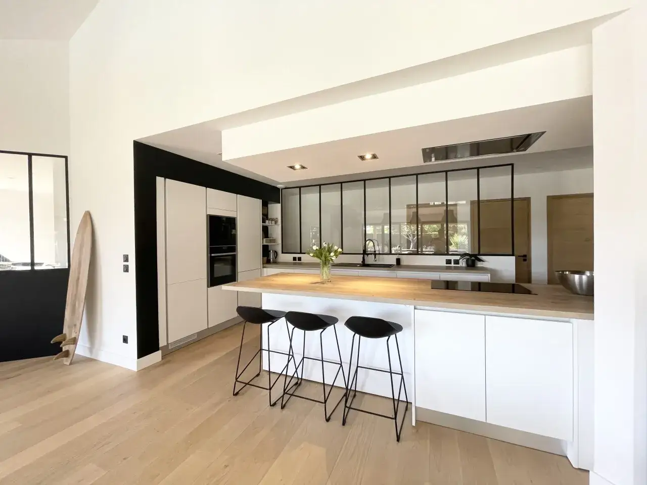 Cuisine ouverte sur salle &agrave; manger moderne, avec &icirc;lot central, tabourets noirs et plan de travail en bois.