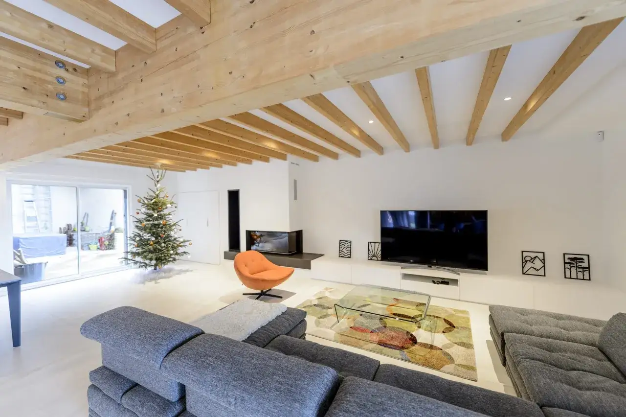 Un salon moderne avec poutre apparente, un sapin de No&euml;l, un canap&eacute; gris et une chemin&eacute;e design.