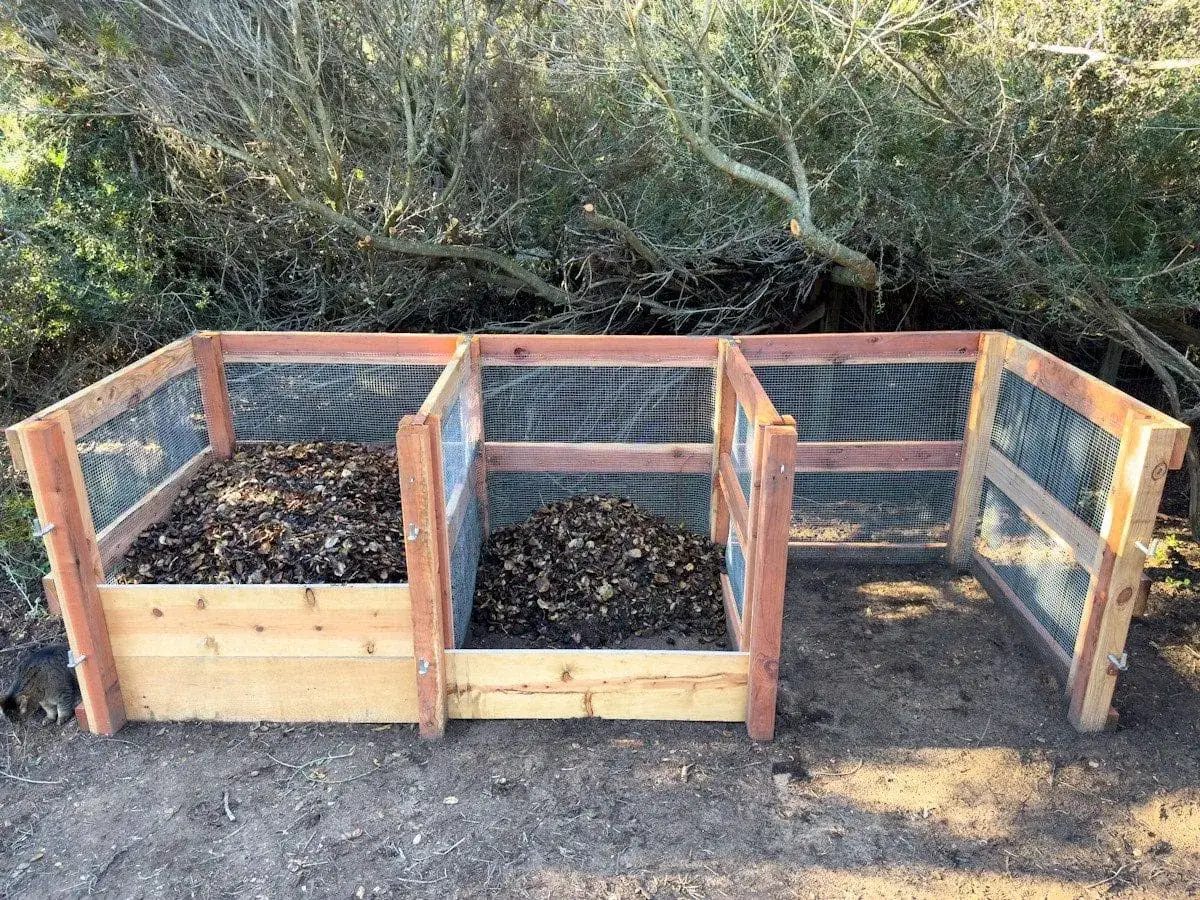Trois bacs en bois et grillage pour fabriquer un composteur. Le premier est rempli de feuilles mortes.