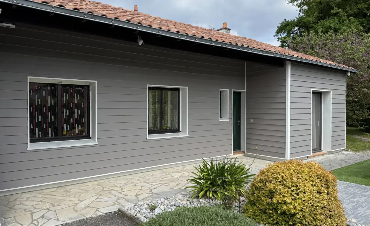 Maison moderne avec bardage gris, fen&ecirc;tres et porte verte. Le rev&ecirc;tement ext&eacute;rieur assure une isolation par l'ext&eacute;rieur efficace.