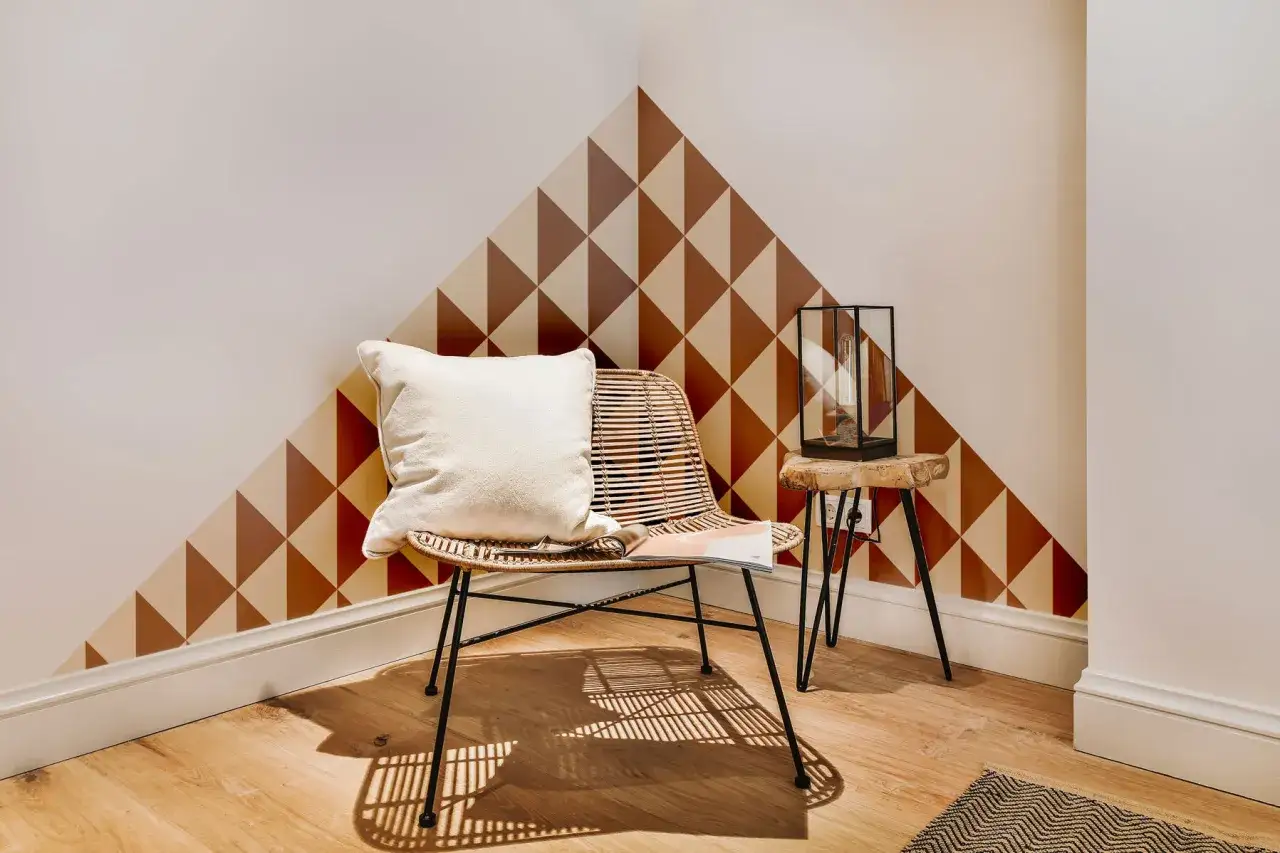 Un coin cosy avec un fauteuil en rotin, un coussin blanc et un motif g&eacute;om&eacute;trique sur le mur. Une belle id&eacute;e motif peinture mur pour un style unique.