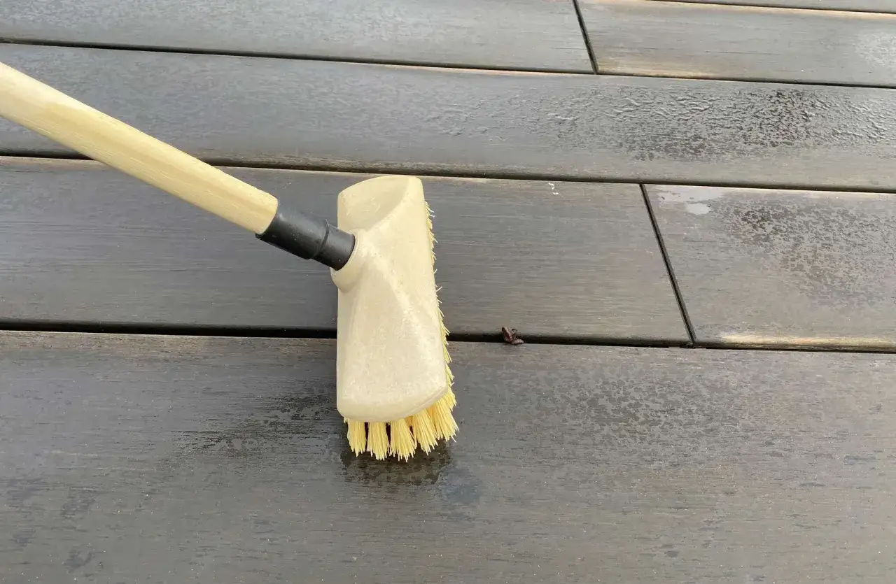 Brosse en action pour nettoyer terrasse bois. L'eau et la saleté s'enlèvent facilement.