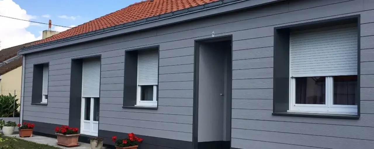Maison moderne avec bardage gris, volets roulants et jardini&egrave;res de fleurs rouges. L'isolation par l'ext&eacute;rieur assure confort et esth&eacute;tique.