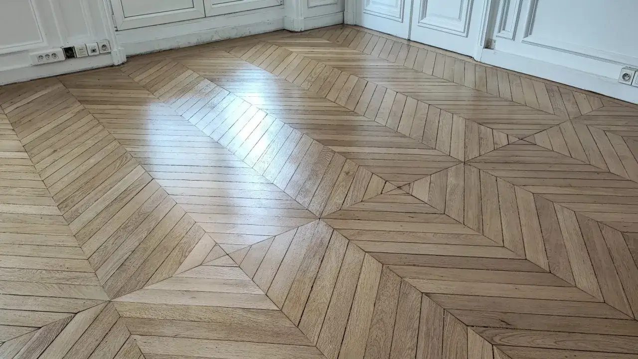Parquet ancien en bois clair, motif géométrique en losanges et chevrons. Une rénovation qui redonne vie à ce sol d'exception.