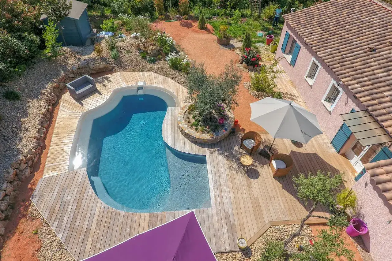 Belle terrasse bois autour d'une piscine sans margelle, avec mobilier de jardin et parasol. Un coin paisible pour se détendre.
