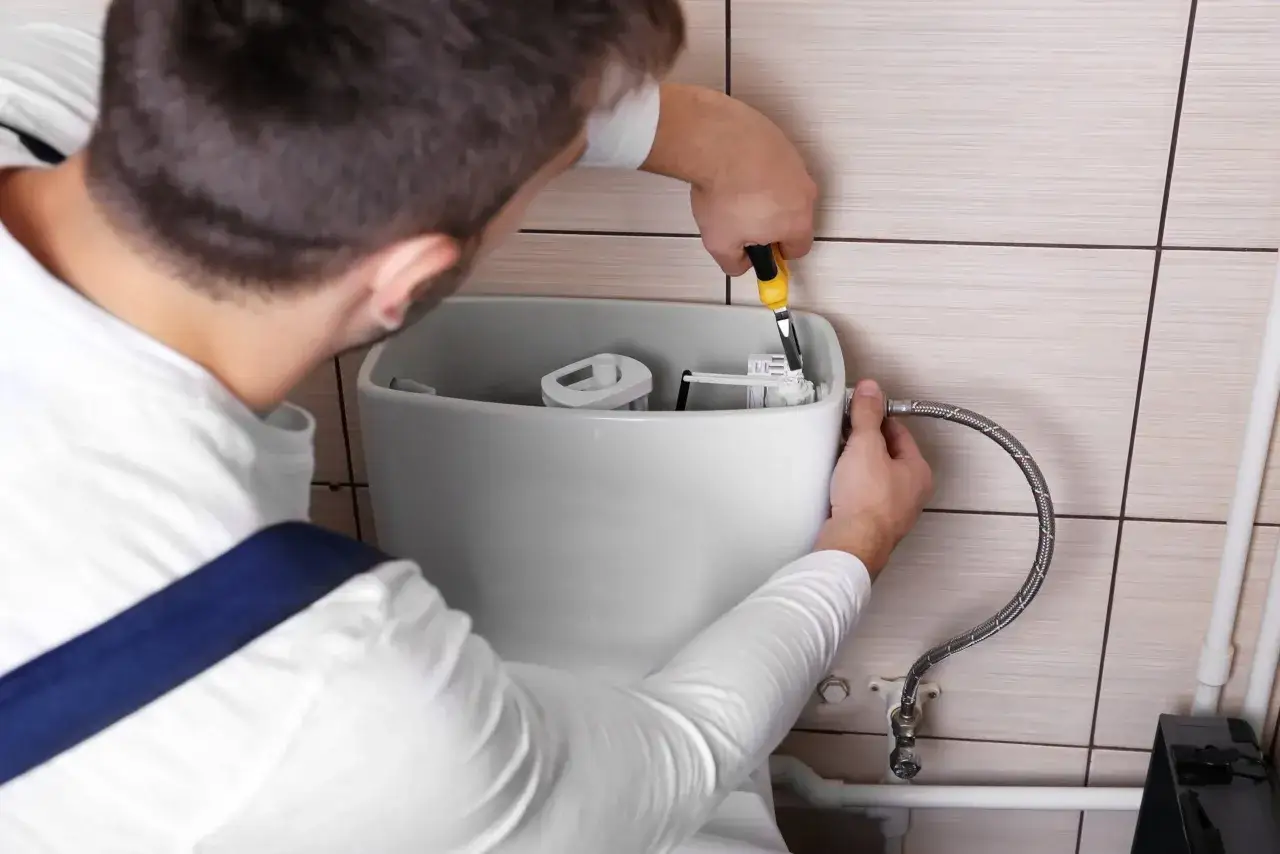 Un plombier utilise une pince pour changer le m&eacute;canisme de chasse d'eau d'une cuvette de toilette.