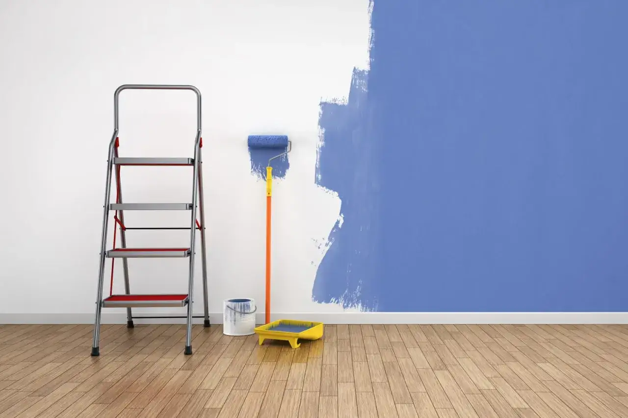 Échelle, rouleau et bac de peinture pour un projet de peinture pour papier peint. Le mur est partiellement peint en bleu.