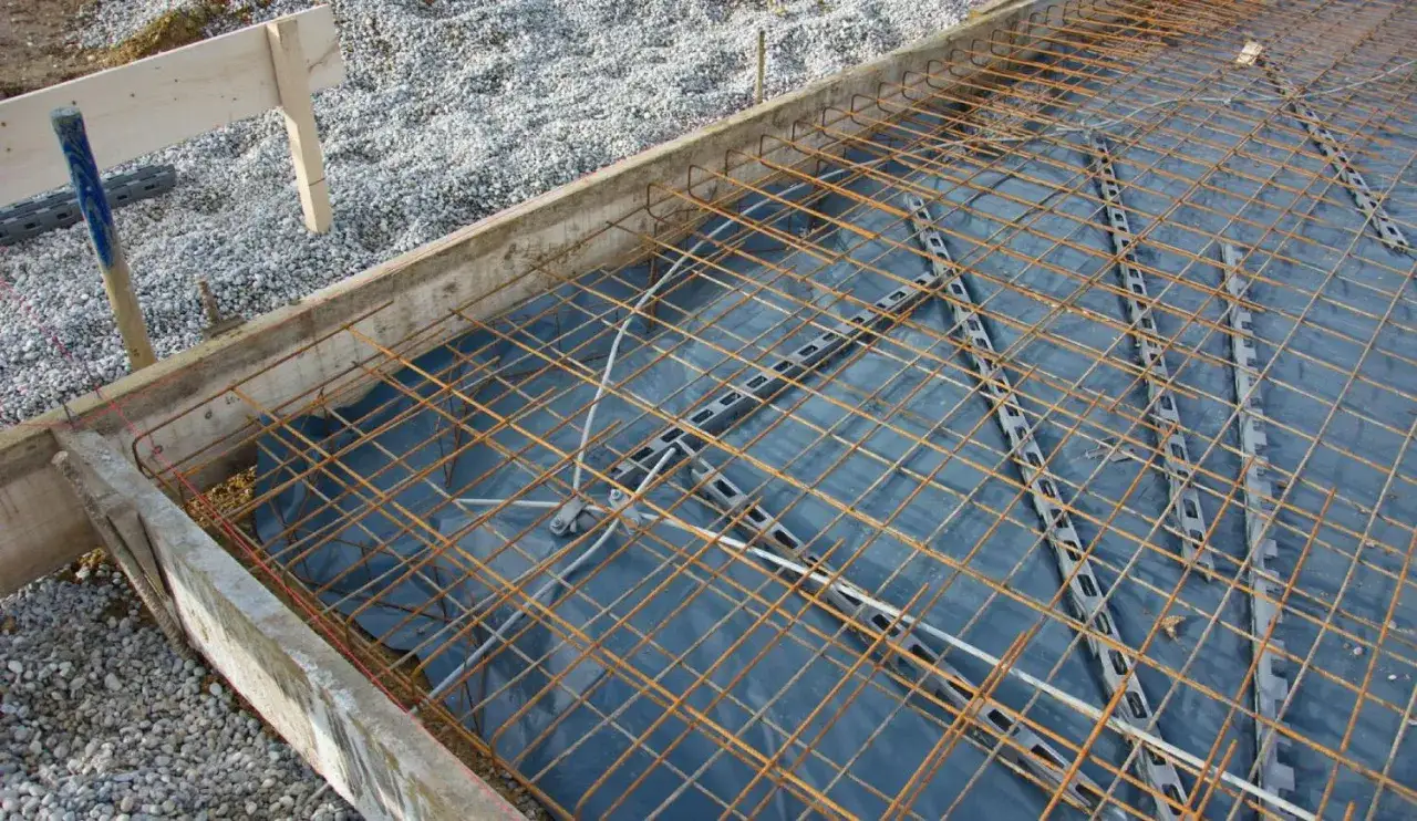 Préparation du coffrage pour une dalle béton. Une armature métallique est posée sur une bâche bleue, prête à être coulée.