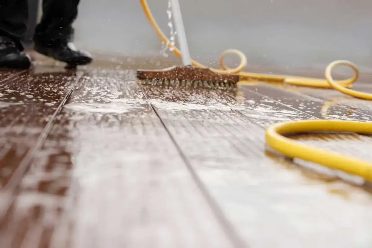 Nettoyage dalle terrasse : une brosse frotte le bois mouill&eacute;, une eau savonneuse coule.