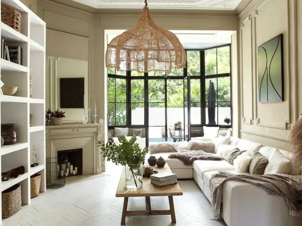 Salon lumineux au style bohème chic maison, avec canapé blanc, suspensions en rotin, cheminée et grandes fenêtres donnant sur le jardin.